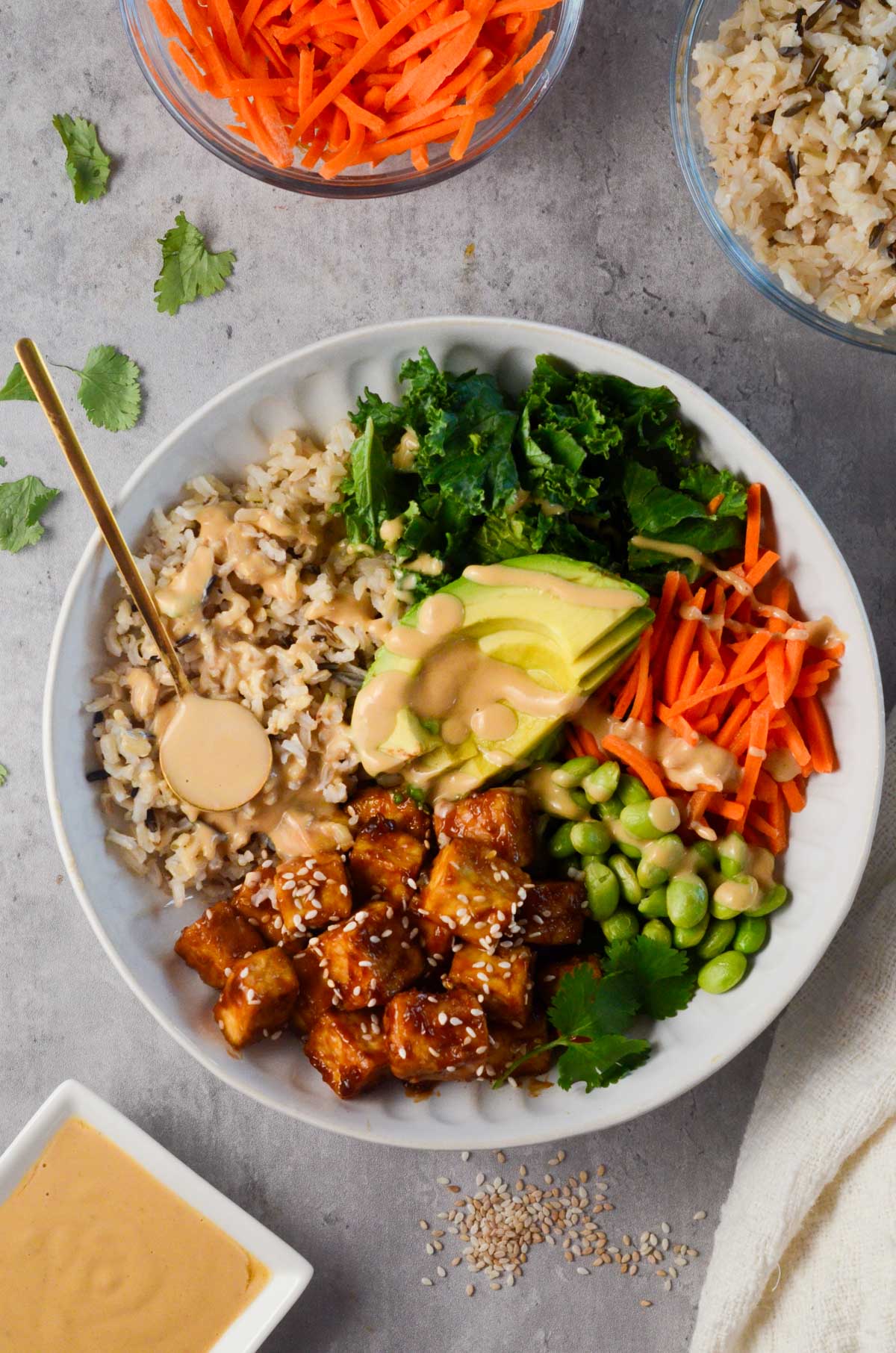 A Buddha Bowl of Asian tofu salad with carrots and sesame ginger dressing, topped with avocado.
