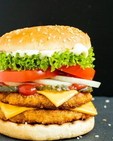 Burger bun with two patties, cheese in between, pickled cucumber slices, onion slices, tomato and ruffled lettuce.