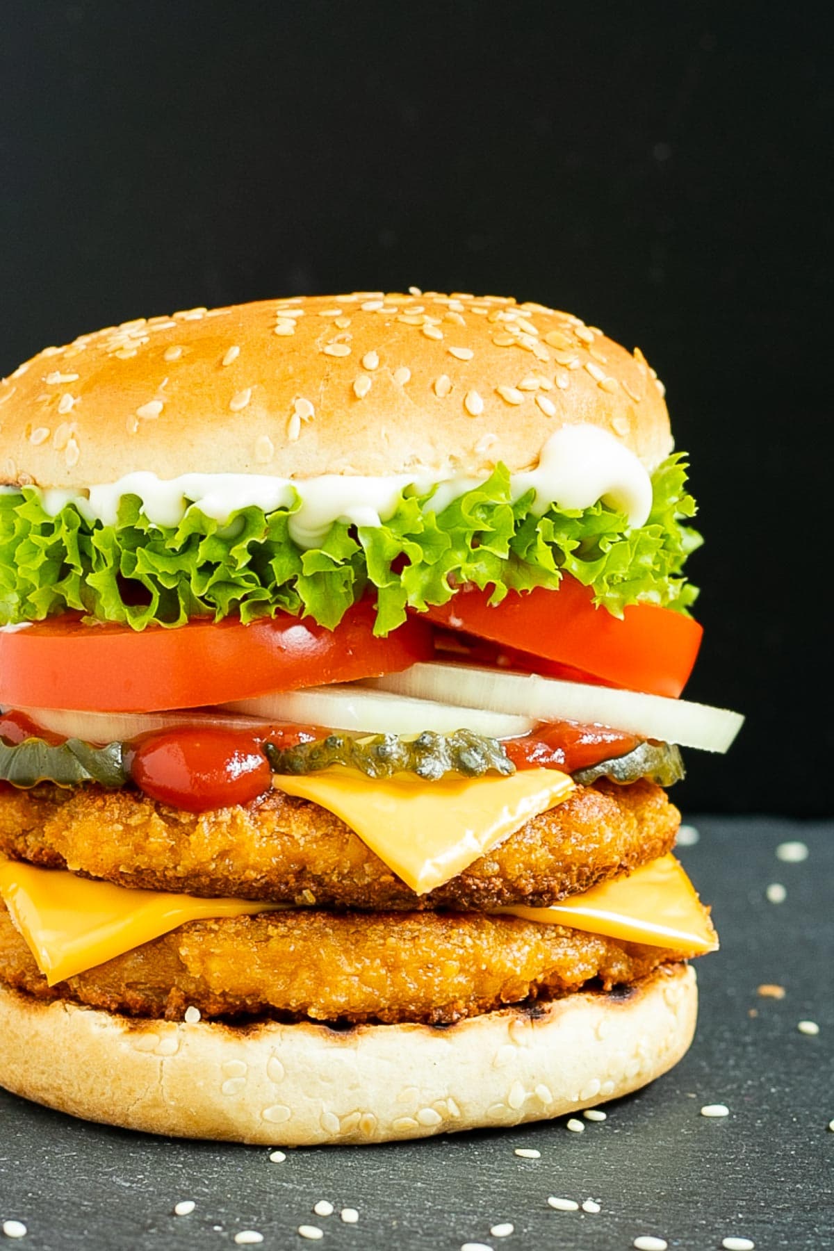 Burger bun with two patties, cheese in between, pickled cucumber slices, onion slices, tomato and ruffled lettuce.