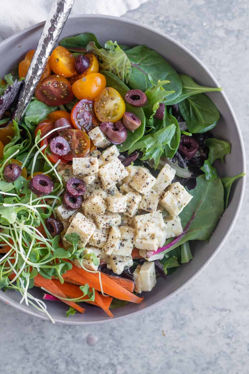 A bowl loaded with white tofu cubes covered in dried herbs and lots of colorful veggies and leafy greens.
