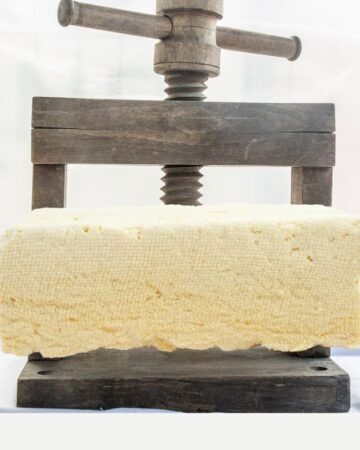 Tofu is being pressed with a wooden press