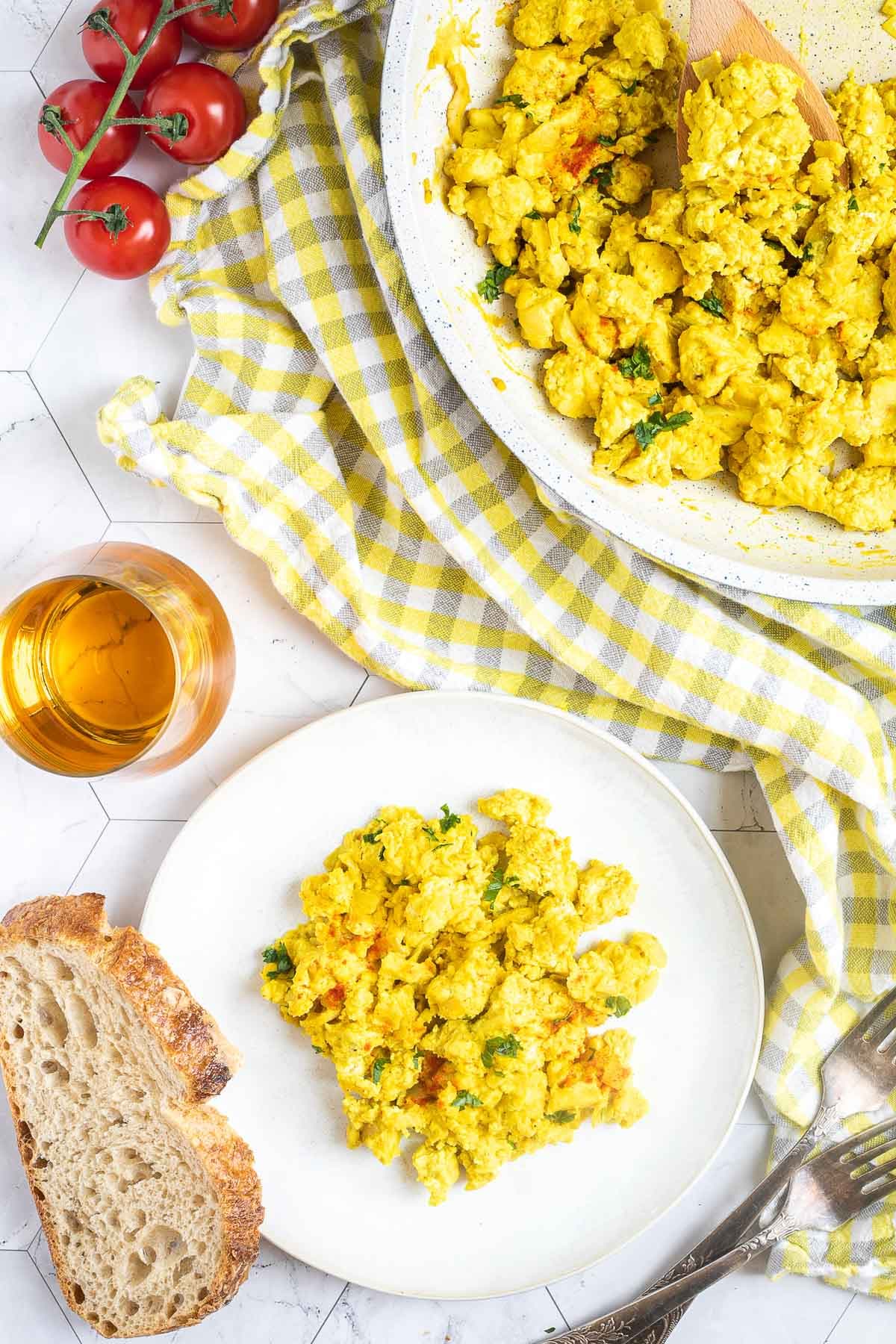 Vibrant yellow scrambled tofu is served on a small white plate. Leftovers are in a white frying pan next to it.