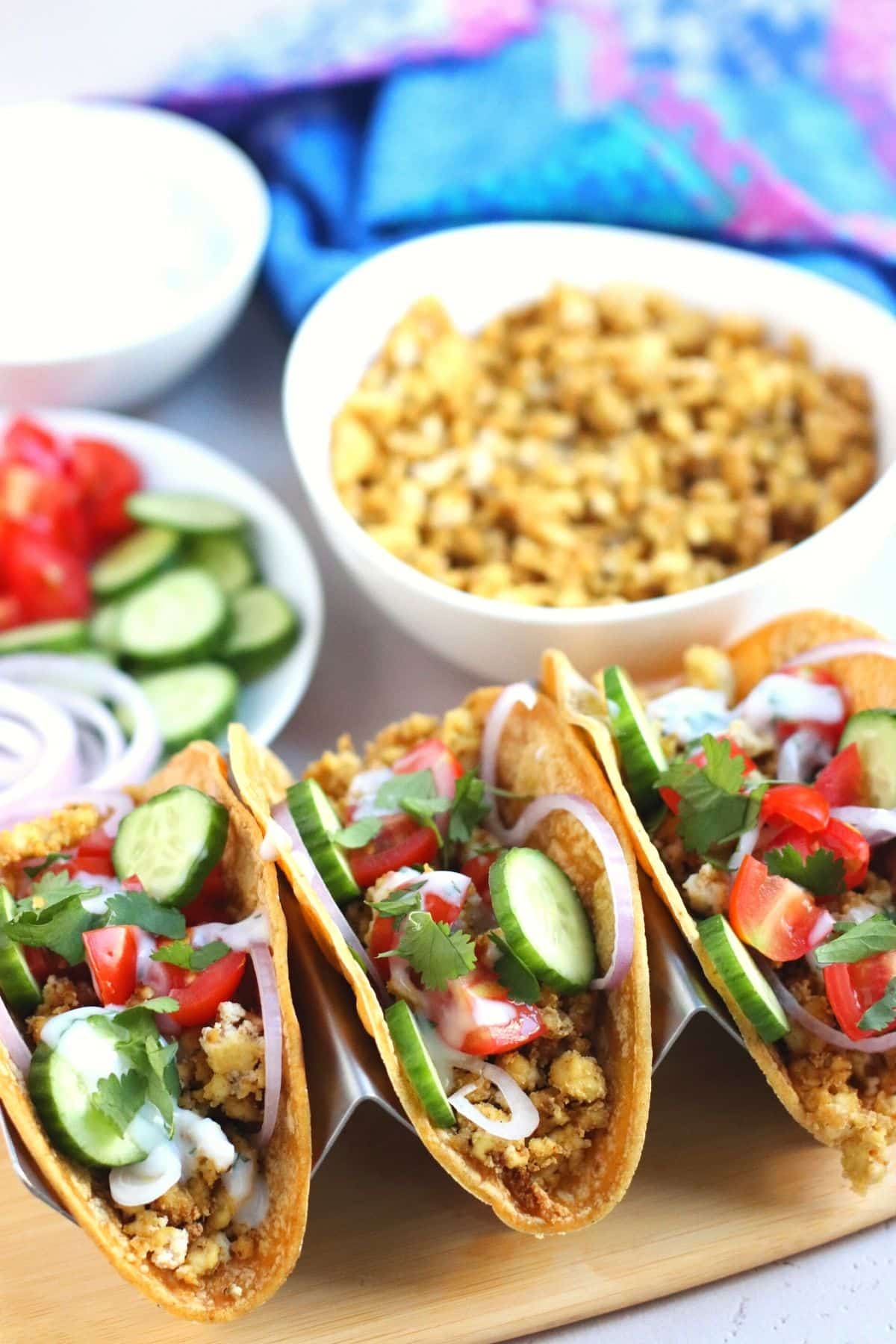 Tofu tacos on a platter with bowl of filling, vegetables toppings, and sauce in the background.