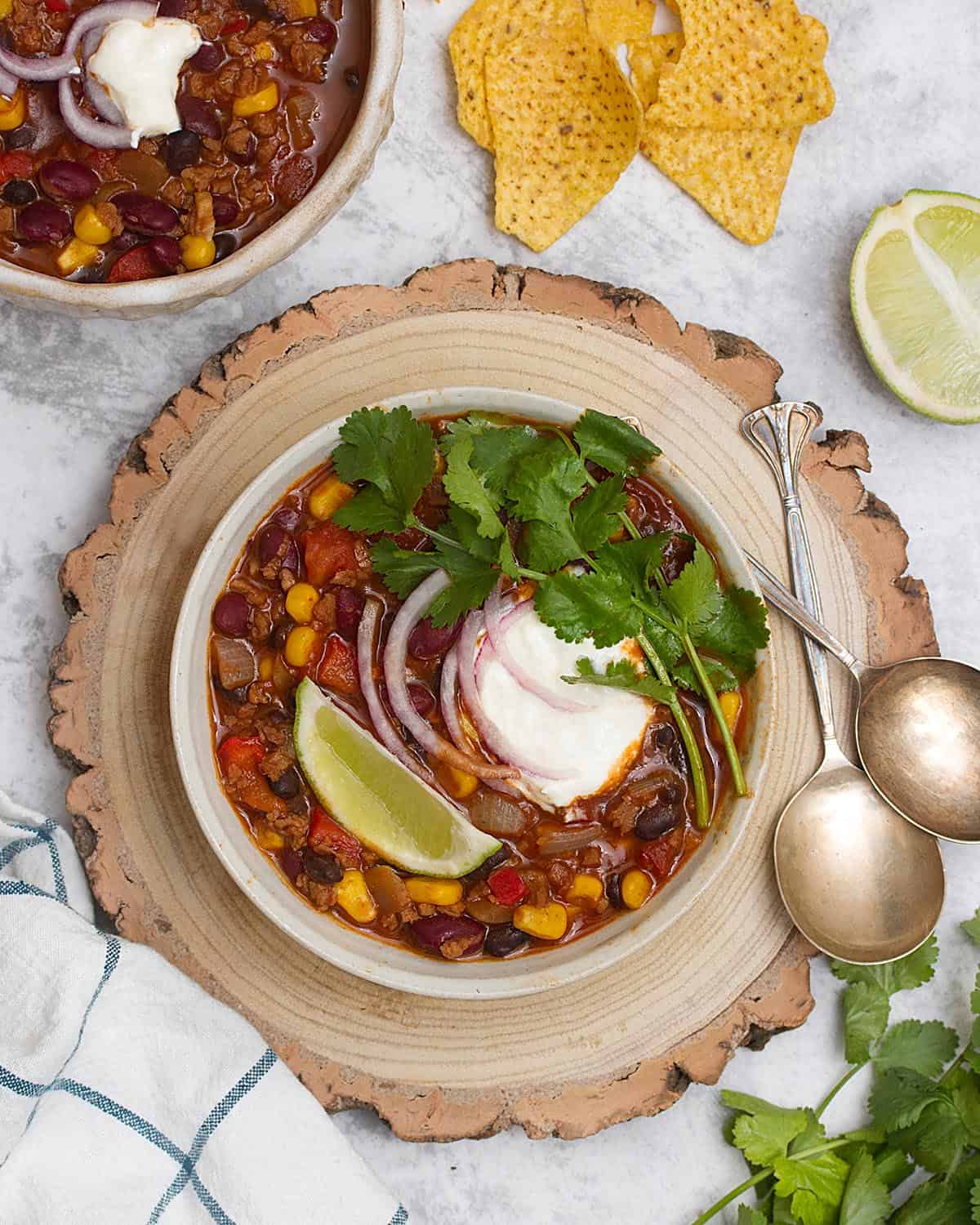 Two bowls of TVP chili with corn tortillas and sour cream.