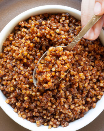 Small white round bowl on a brown plate with brown bits. A hand is holding a spoon and dunking in the middle.