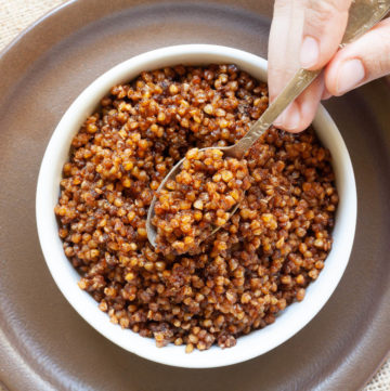 Small white round bowl on a brown plate with brown bits. A hand is holding a spoon and dunking in the middle.