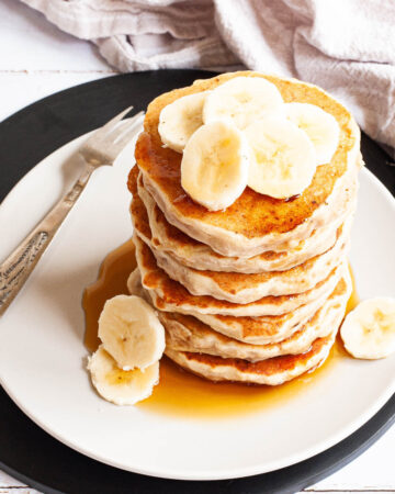 White plate with a stack of pancakes topped with banana slices