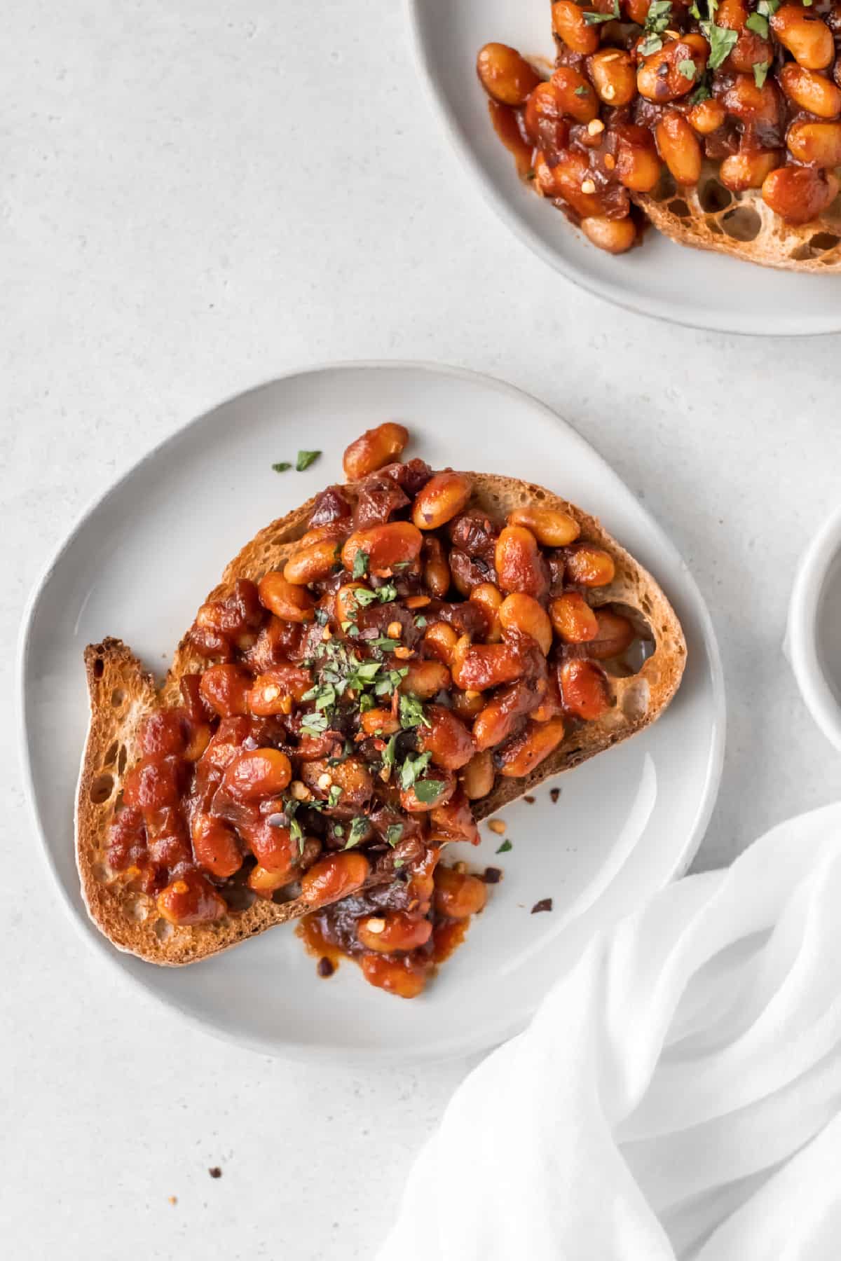 A slice of crusty bread on a white plate topped with beans in red sauce.