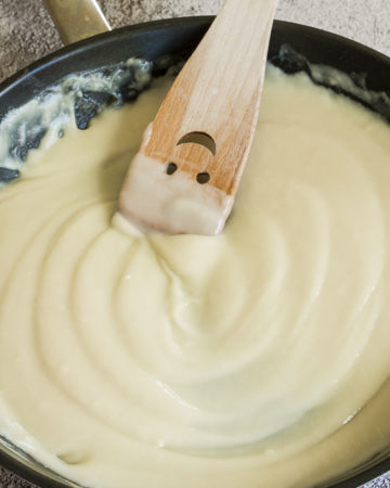 White sauce in black frying pan with a smiling wooden spatula in the middle