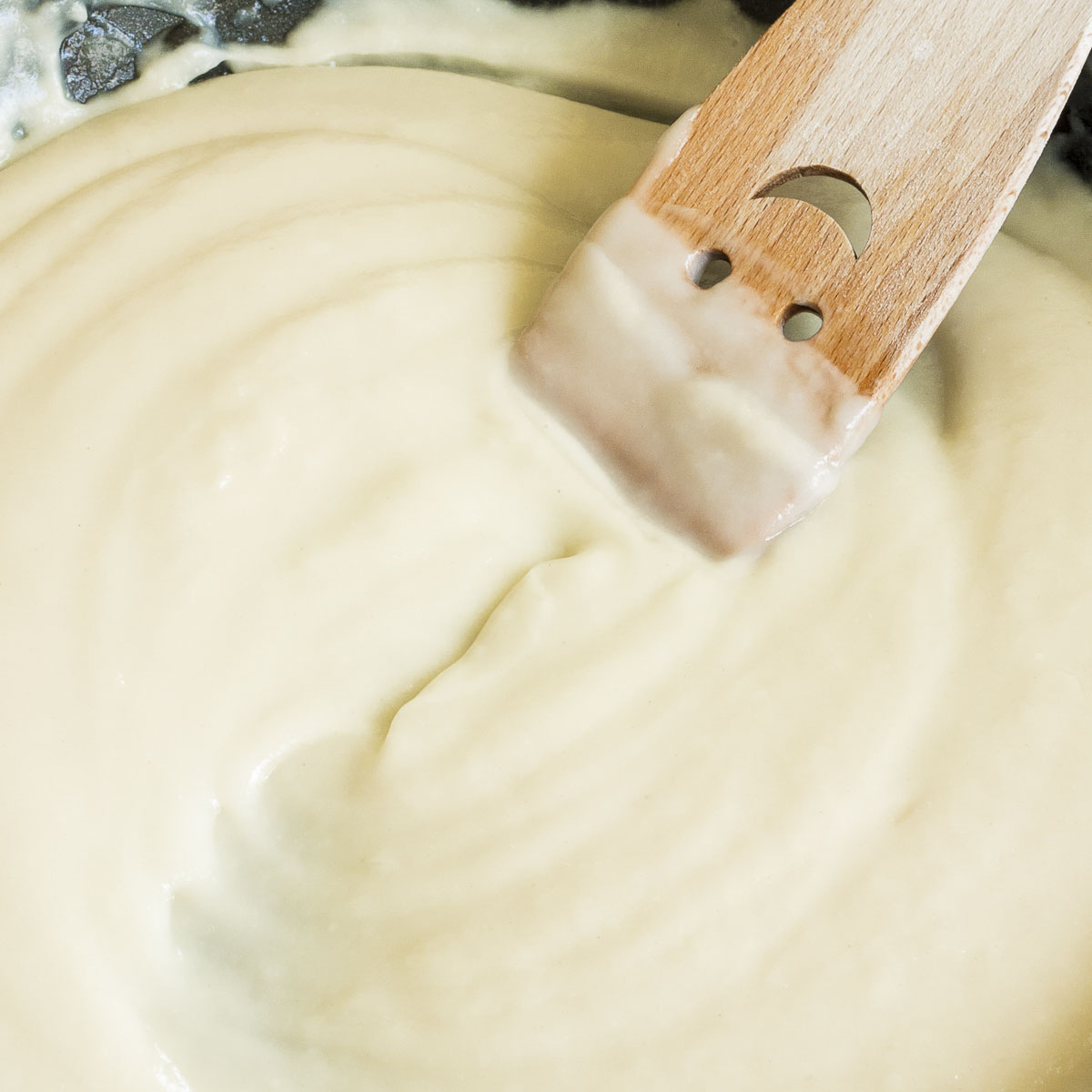 White sauce in black frying pan with a smiling wooden spatula in the middle