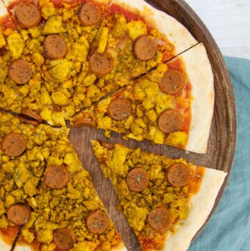 Pizza with scrambled egg-like yellow crumbles and sausage slices.