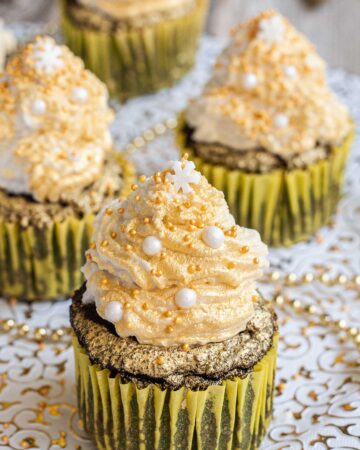 4 dark brownie cupcakes in yellow cupcake liner topped with a white frosting sprayed with gold and sprinkled with gold and white pearl sprinkles and a snowflake one on top.