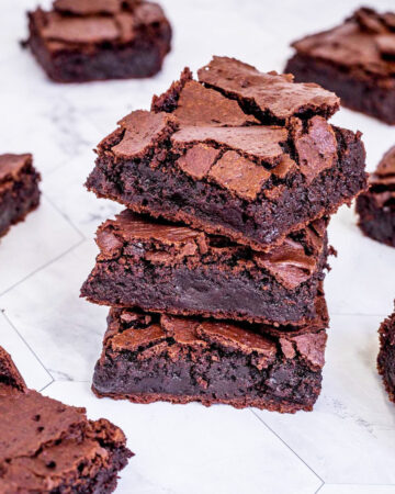 3 square brownies on top of each other with fudgy middle and crackly top. Several more scattered around.