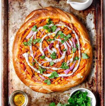 Pizza with tomato sauce, orange chicken-like pieces, red onion slices, corn, and melted cheese. Sprinkled with fresh chopped herbs.