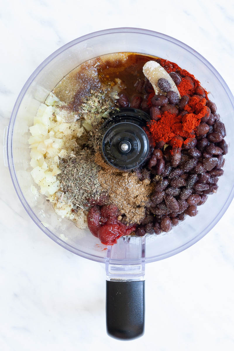 A food processor from above showing black beans, chopped onion, different colored spices