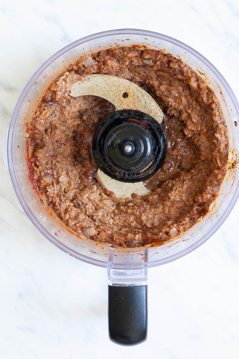 A food processor from above showing dark brown chunky sauce