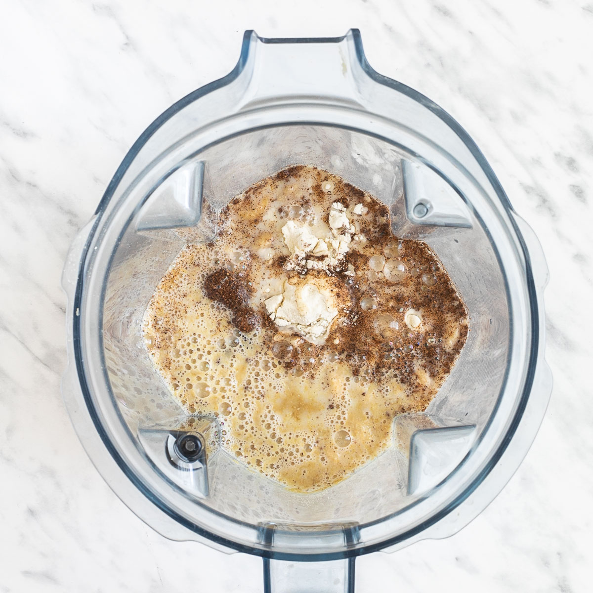 A blender from above with cashew nuts, milk, yellow flakes, nutmeg, and salt.