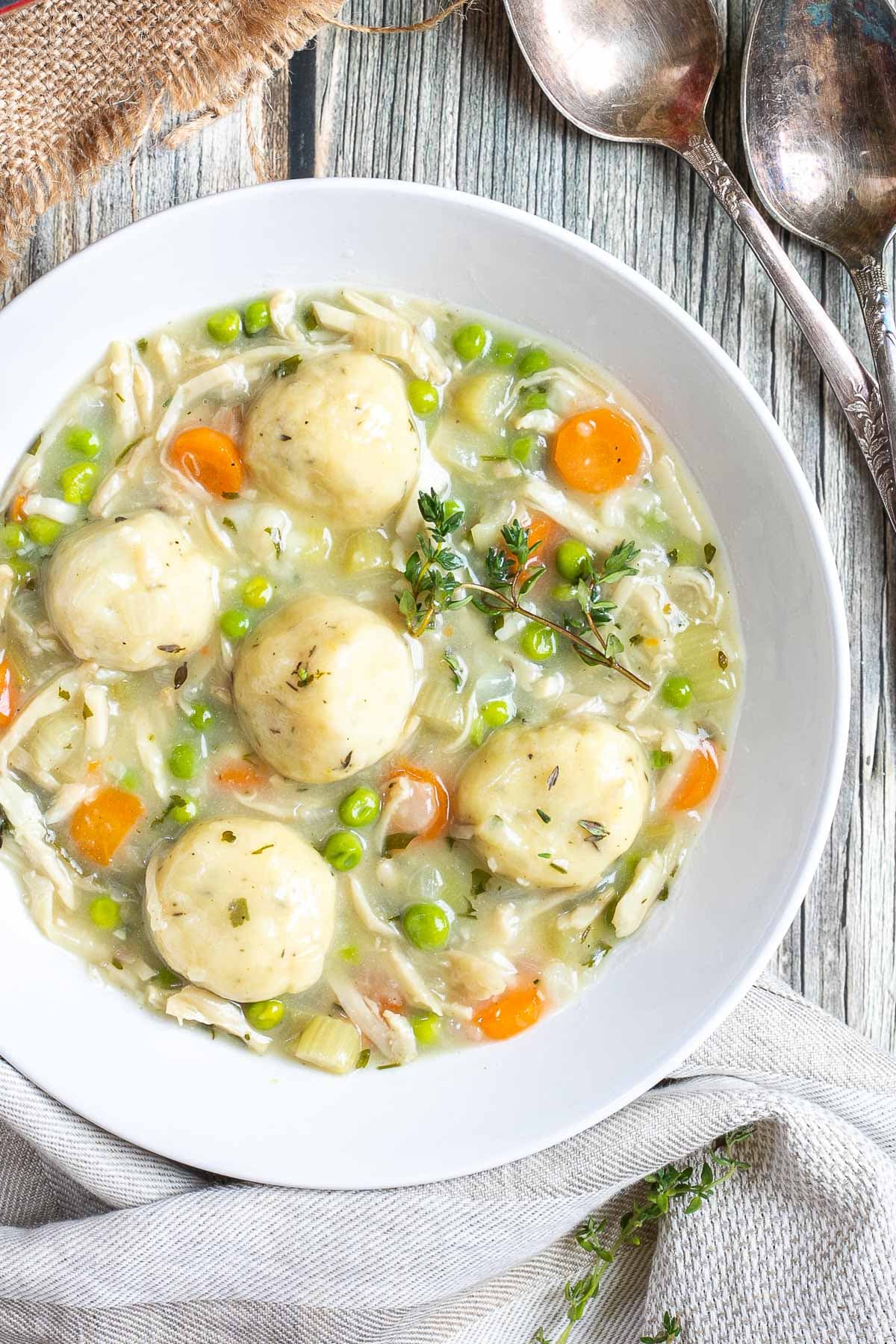 A white plate with dumplings, chopped veggies, shredded mushroom pieces in place of chicken, green herbs in a thick, white stew.