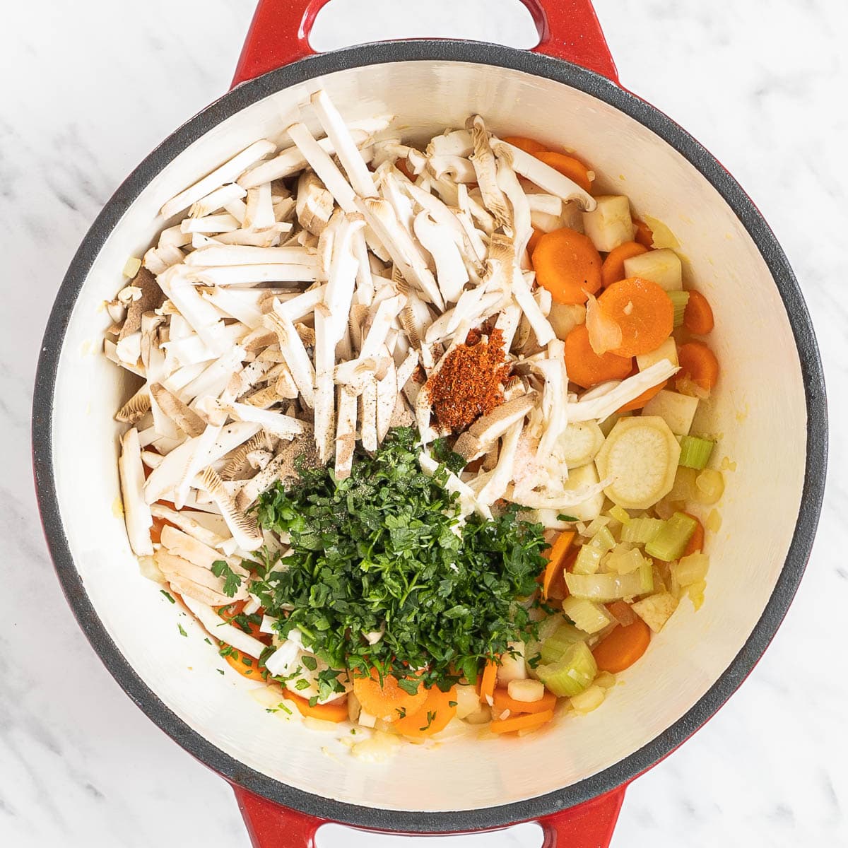 Red Dutch oven with sliced carrots, chopped parsnip, chopped celeriac, celery stalk, shredded oyster mushrooms, chopped herbs.