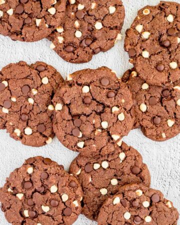 Dark brown cookies with white and dark chocolate chips on a white surface.