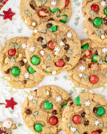 Light brown cookies with red and green m&ms, chocolate chips, tiny white sugar snowflakes, and tiny green pine trees.