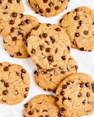 Lots of chocolate chip cookies on a white wooden surface.