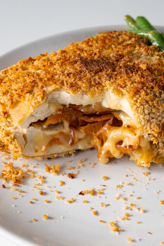 A crispy piece of tofu cordon bleu on a plate with green beans.