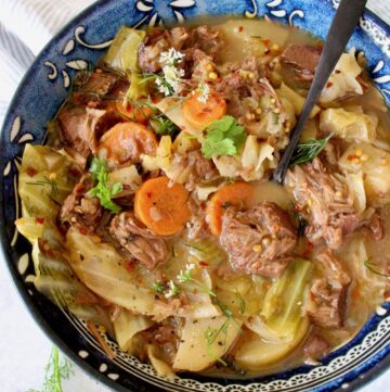 Brown meaty jackfruit pieces, carrot, potatoes and cabbage in a brow stew served in a blue bowl.