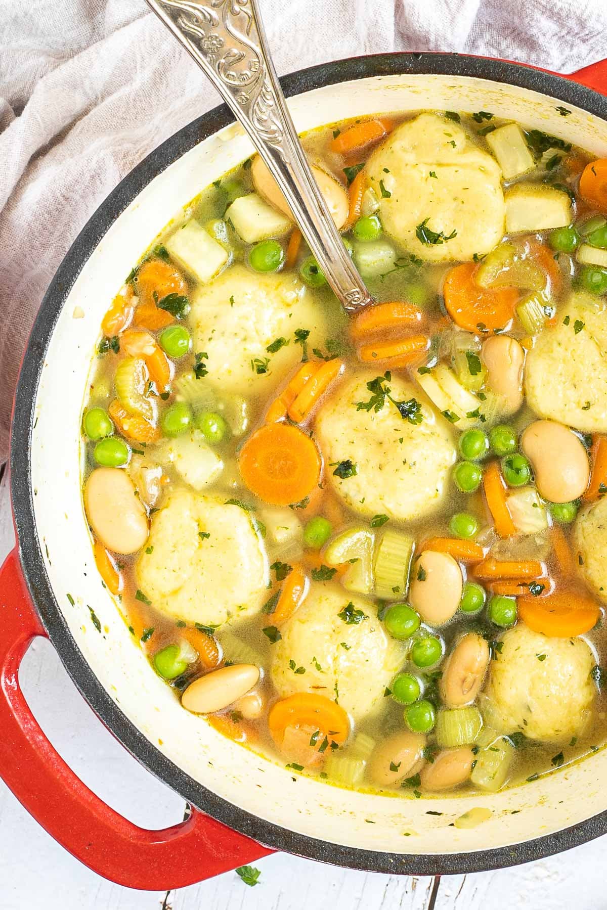 Dutch oven with dumplings, chopped veggies, green herbs, white beans, and green peas in a vegetable broth soup.