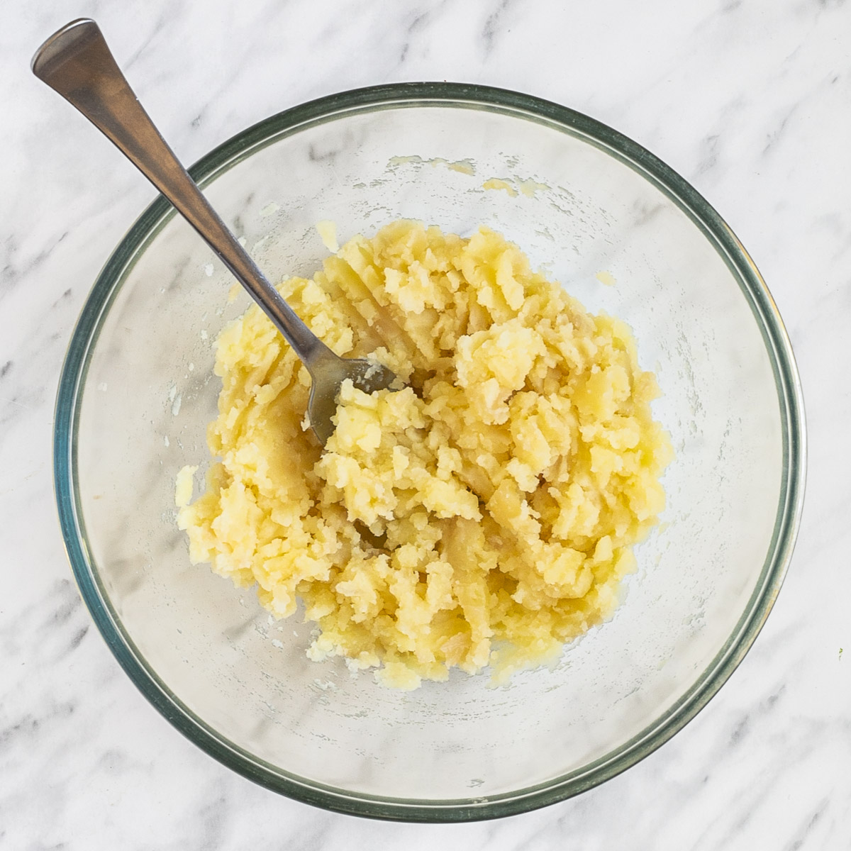 A glass bowl with mashed potato and a fork.