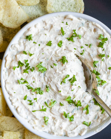 White bowl with white thick creamy sauce in it sprinkled with fresh green herbs. A spoon is places in the middle.