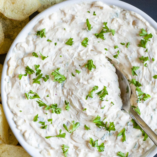 White bowl with white thick creamy sauce in it sprinkled with fresh green herbs. A spoon is places in the middle.