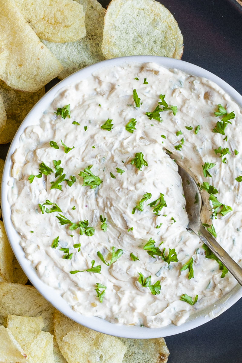 White bowl with white thick creamy sauce in it sprinkled with fresh green herbs. A spoon is places in the middle.