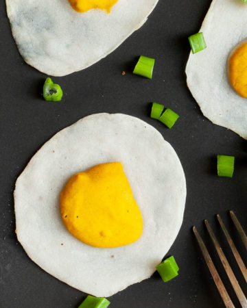 3 fried egg lookalike with white and yolk part on a black plate sprinkled with green spring onion rings.