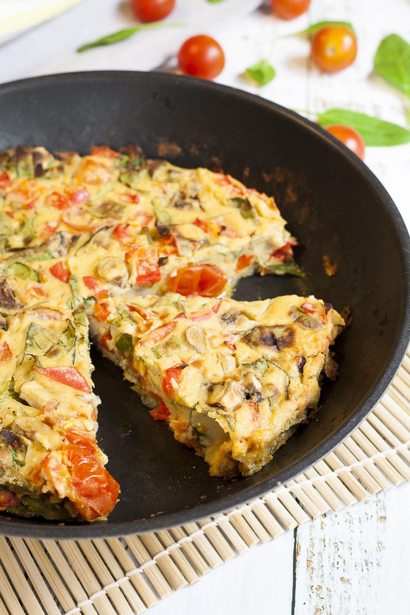 A frying pan with frittata, chopped veggies in an eggy batter.