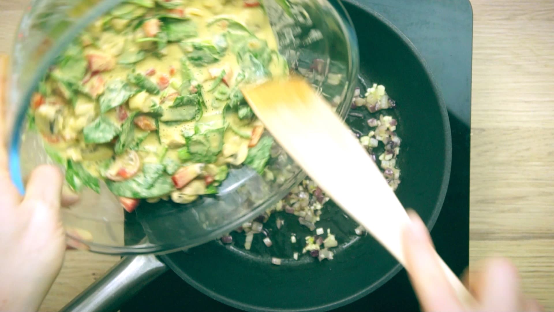 A hand is pouring a yellow batter full of chopped veggies to a frying pan.