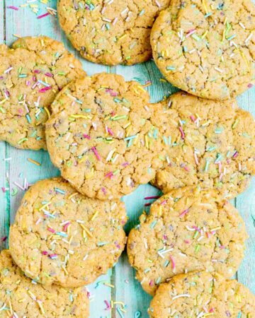 Light brown cookies with rainbow sprinkles on a blue wooden surface.