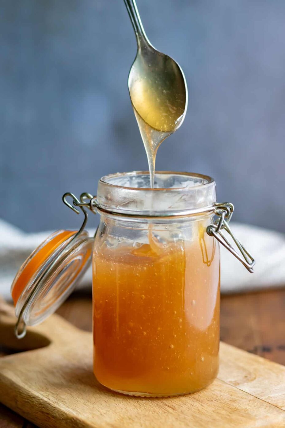 A mason jar of orange brown syrup and a spoon is taking some.