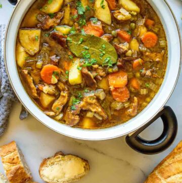 Large black and white pot with vegetable chunks and seitan pieces in a brown stew sauce topped with freshly chopped herbs.