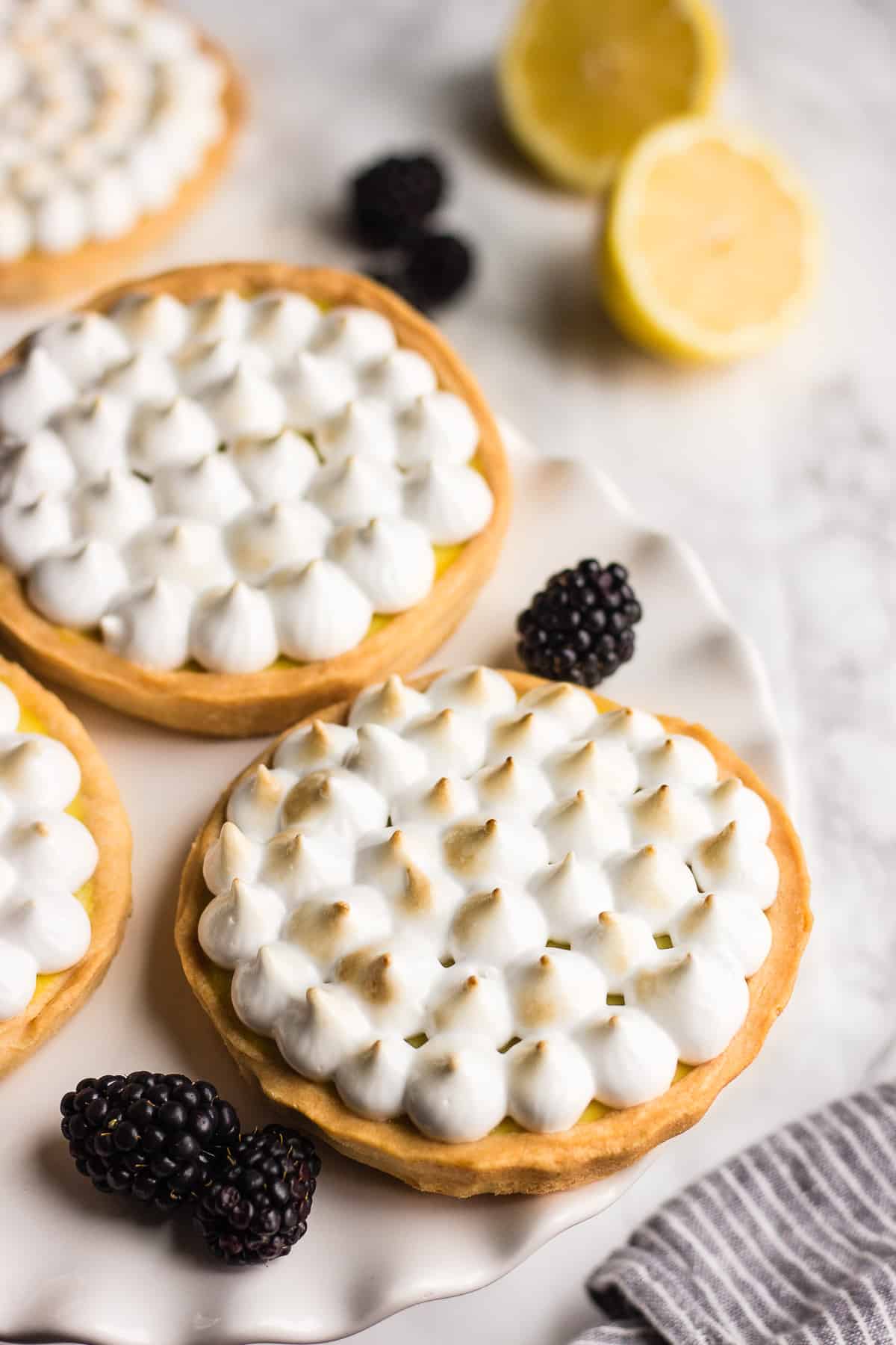Vegan lemon tartlets with blackberries around it and lemon in the background.