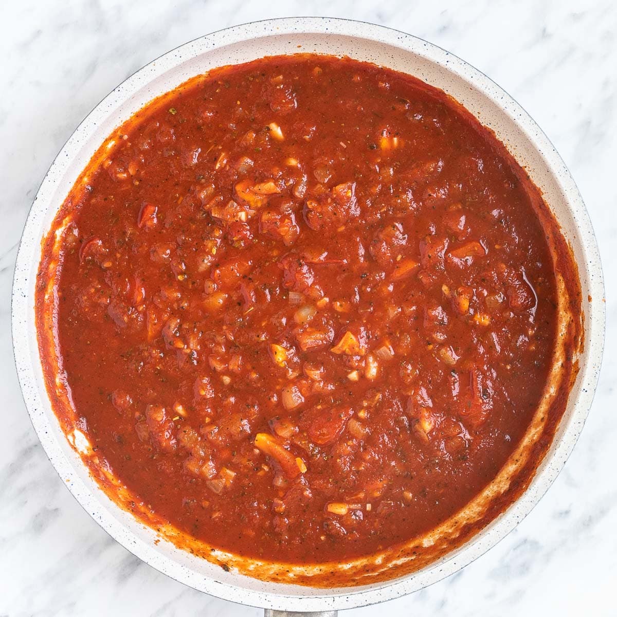 A chunky red sauce in a white frying pan.