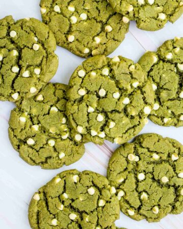 Lots of vibrant green cookies with white chocolate chips on a marble surface.