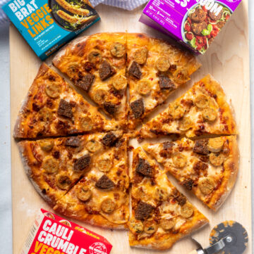 Sliced pizza with red sauce, melted cheese, crumbles, sausage slices, and patty pieces.