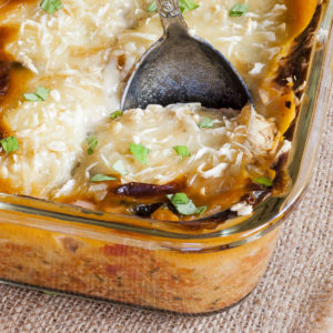 The corner of a glass dish up close with a serving spoon. The dish is full of yellow-red-brown food topped with chopped green herbs
