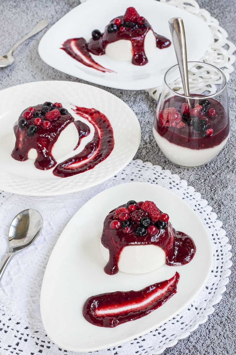 3 white plates and a glass with white panna cotta topped with a thick purple sauce and different berries.