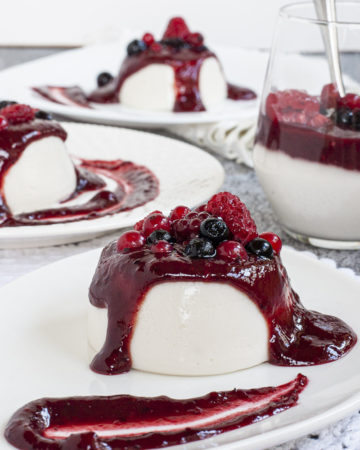 3 white plates with white panna cotta topped with a thick purple sauce and different berries.