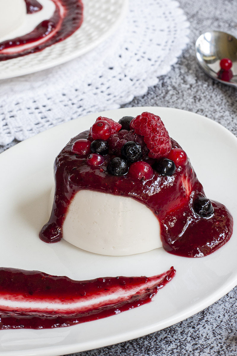 A white plate with white panna cotta topped with a thick purple sauce and different berries.