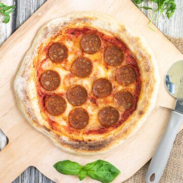 Pizza on a wooden baker's peel topped with tomato sauce, melted cheese and pepperoni slices.