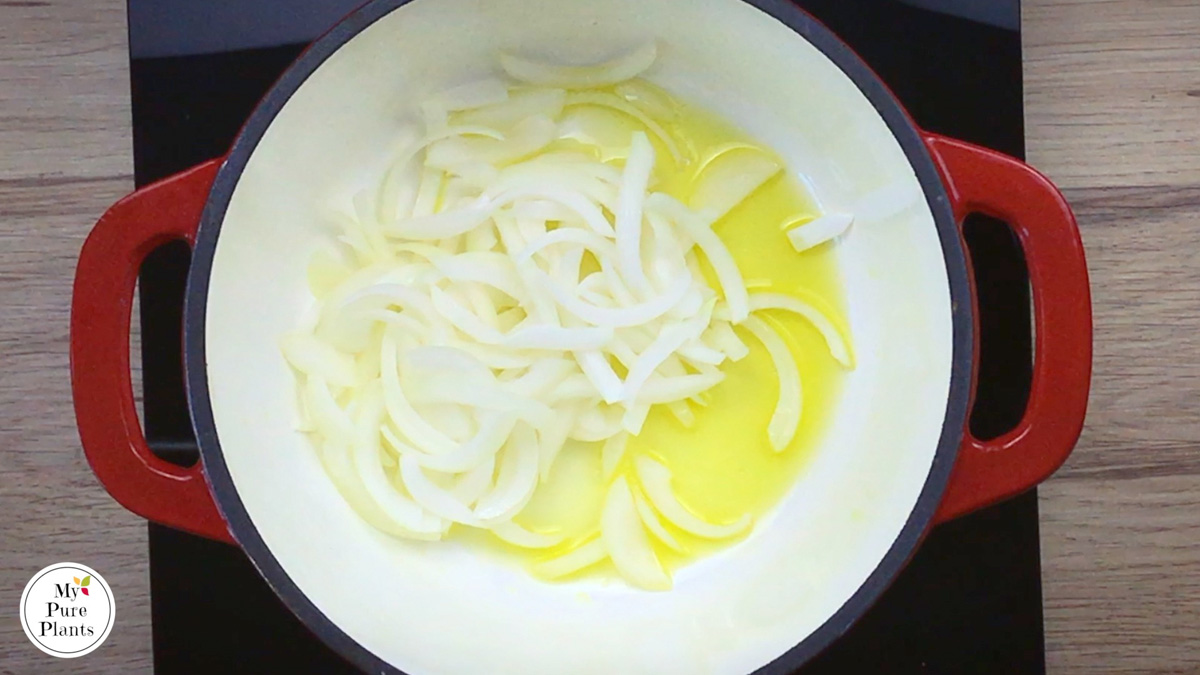 Red-white enameled Dutch oven with oil and sliced onion.