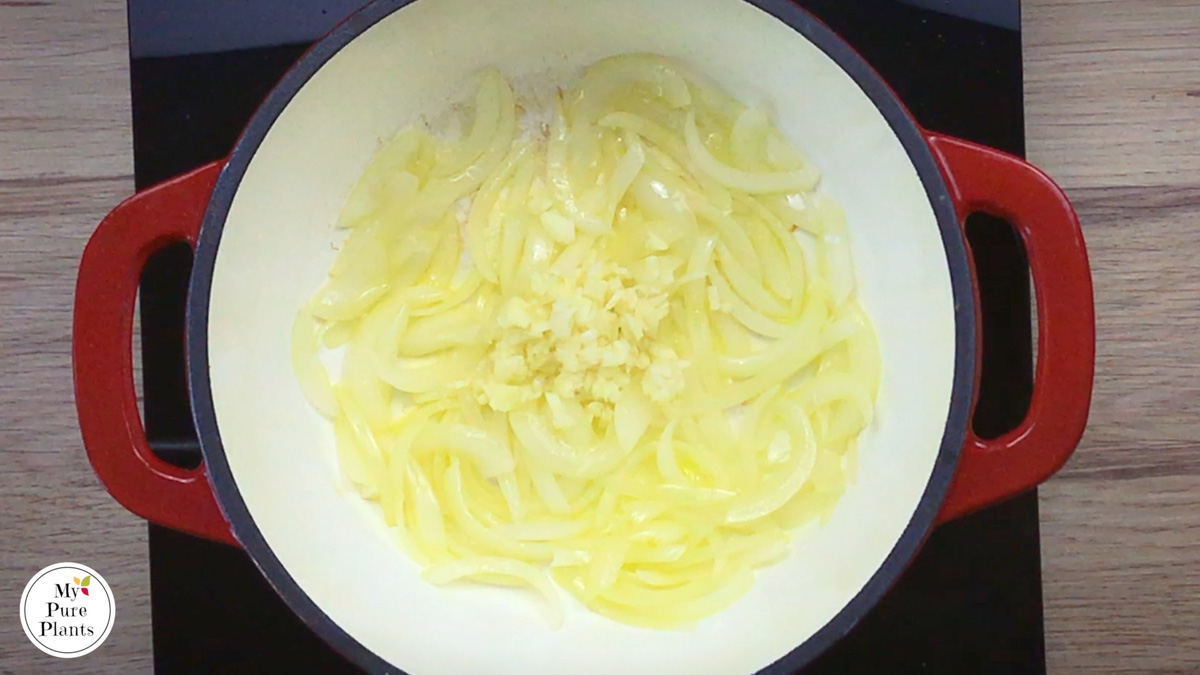 Red-white enameled Dutch oven with lightly cooked sliced onion and a small heap of minced garlic in the middle.